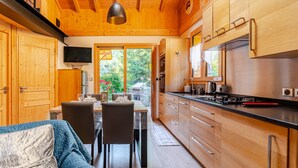A wooden interior with a dining table, chairs, a sofa, and a kitchen area with cabinets and appliances.