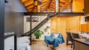 A modern interior with a staircase, a blue armchair, a dining area, and a wooden ceiling.