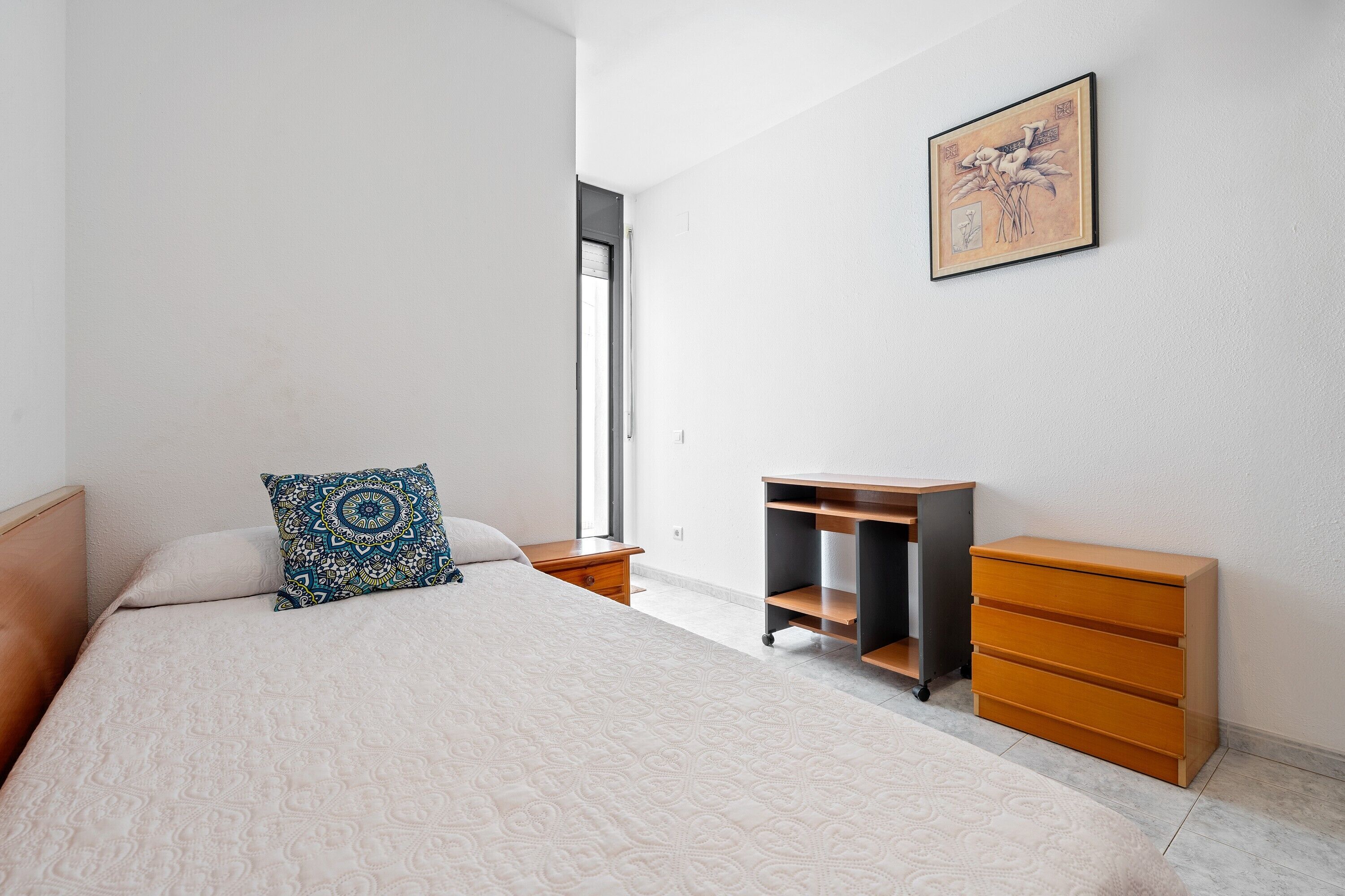 Ein Schlafzimmer mit Bett, Schreibtisch, Kommode und Fenster.
