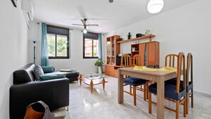 A modern living room with a sofa, coffee table, dining table, chairs, and a ceiling fan.