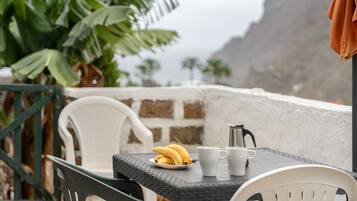 A table with a plate of bananas, two white cups, and a silver pot.
