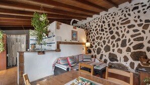 Un intérieur rustique avec un mur en pierre, des poutres en bois au plafond, une table à manger avec un set de table et un canapé agrémenté de coussins à motifs.