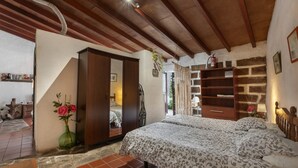 Une chambre à coucher avec un lit, une armoire, un vase vert contenant des fleurs et un mur en briques.