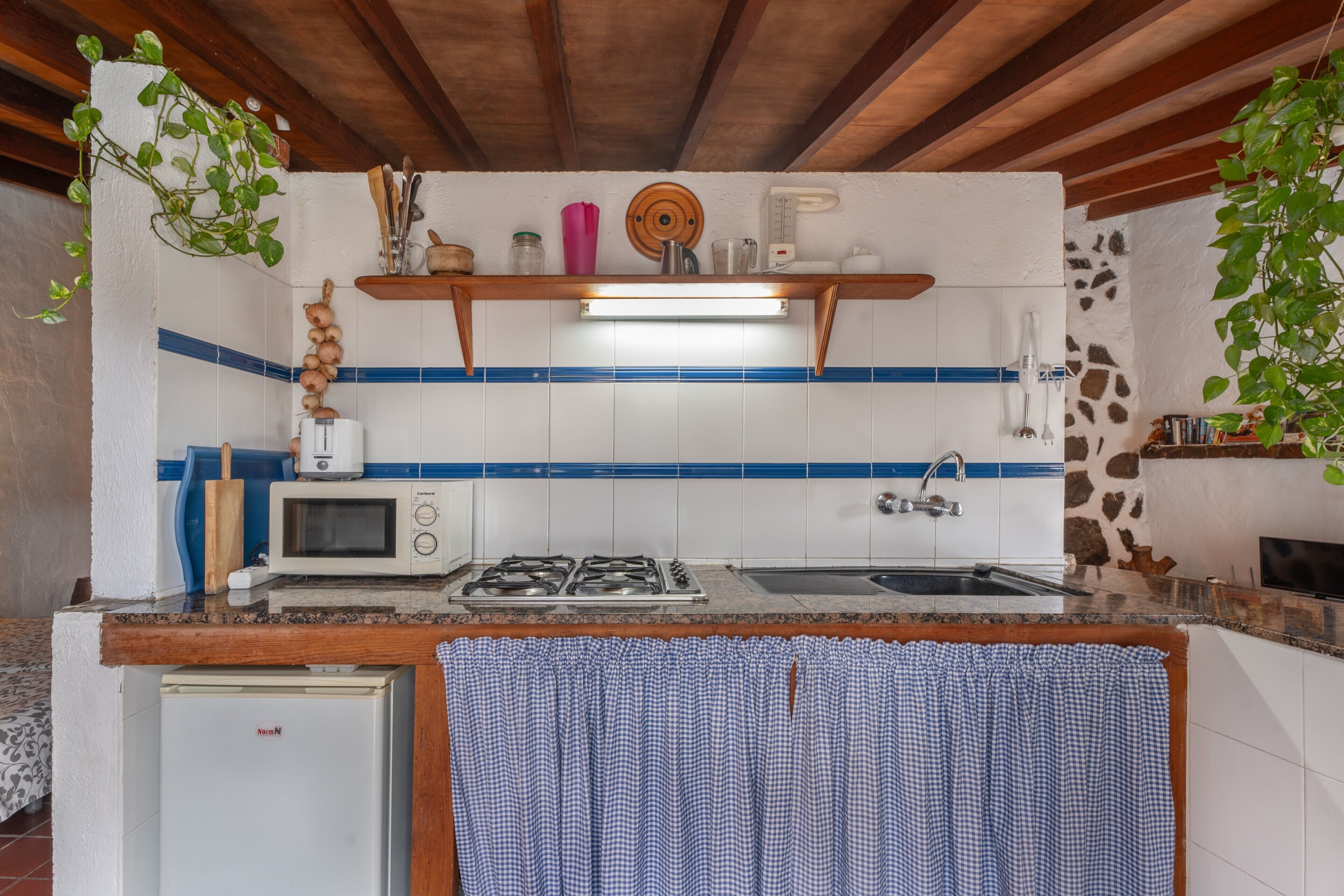 Cocina compacta con microondas, estufa y lavaplatos, vigas de madera en el techo y un refrigerador pequeño.