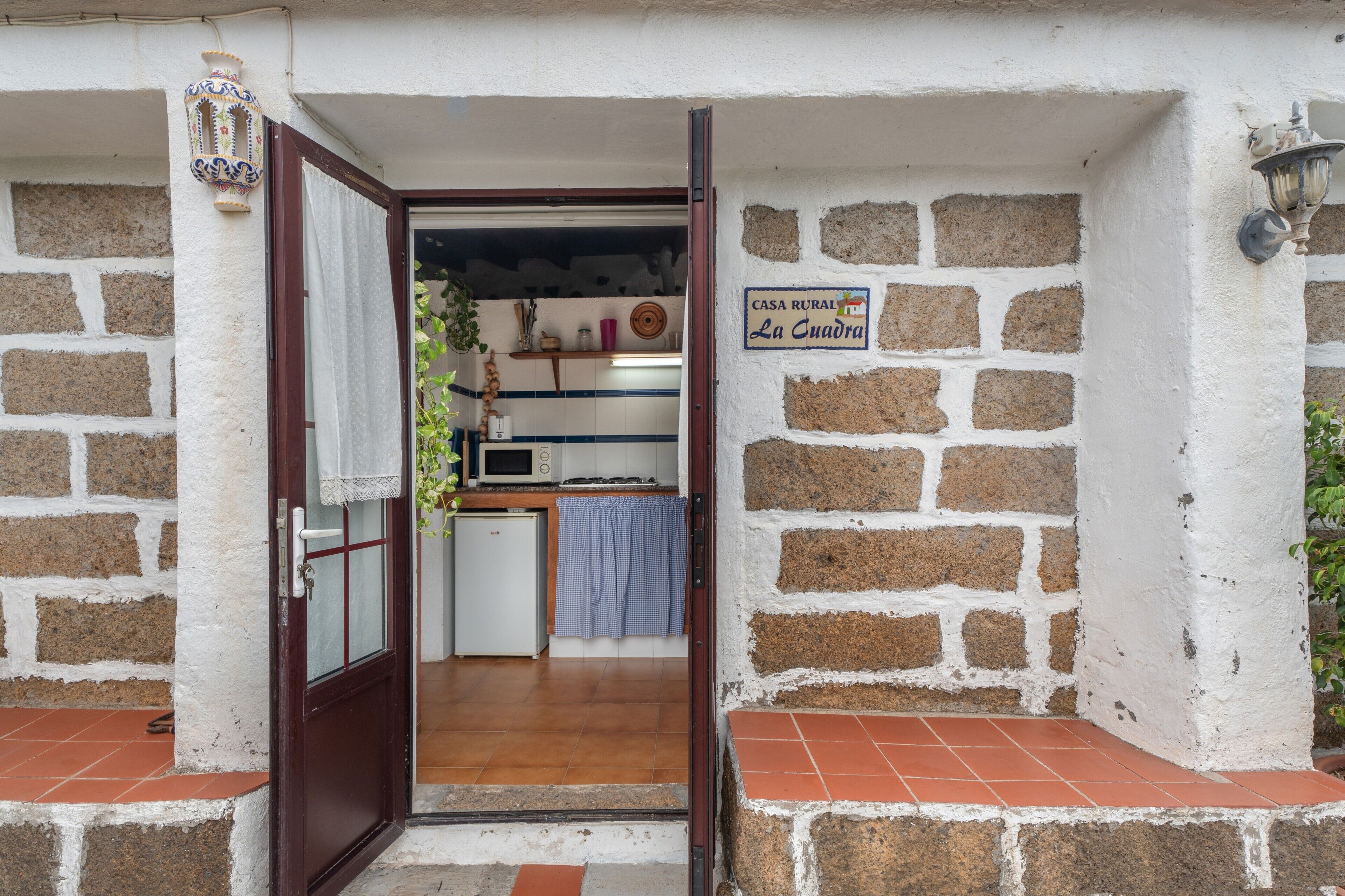 Ein rustikales Haus mit einem Schild, auf dem 'Casa Rural La Cuadra' steht, eine kleine Küche mit einer Mikrowelle und ein Fliesenboden.