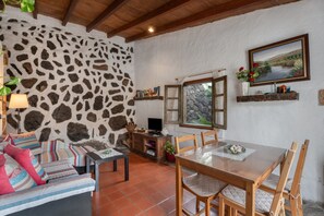 A cozy room with a stone wall, a wooden dining table, and a television. - 'Casa Rural La Cuadra' with Sea Views, Private Terrace and Wi-Fi (Hermigua)