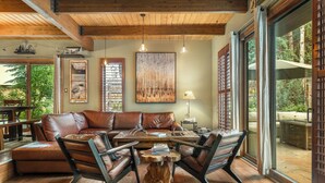A cozy living room with a leather sofa, wooden coffee table, and a large window offering a view of the outdoors. - Private Hot Tub & Pet Friendly + Beds For Any Group Dynamic (Avon)