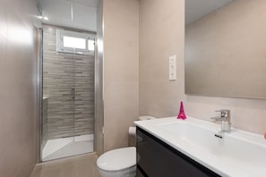 A modern bathroom with a glass shower enclosure, a white toilet, a large white sink with a chrome faucet, and a mirror above the sink.