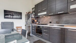 A modern kitchen with dark cabinetry, a stainless steel refrigerator, a gas stove, and a large window. - House of Flowers holiday home with balcony and Wi-Fi (Montopoli vald’arno)