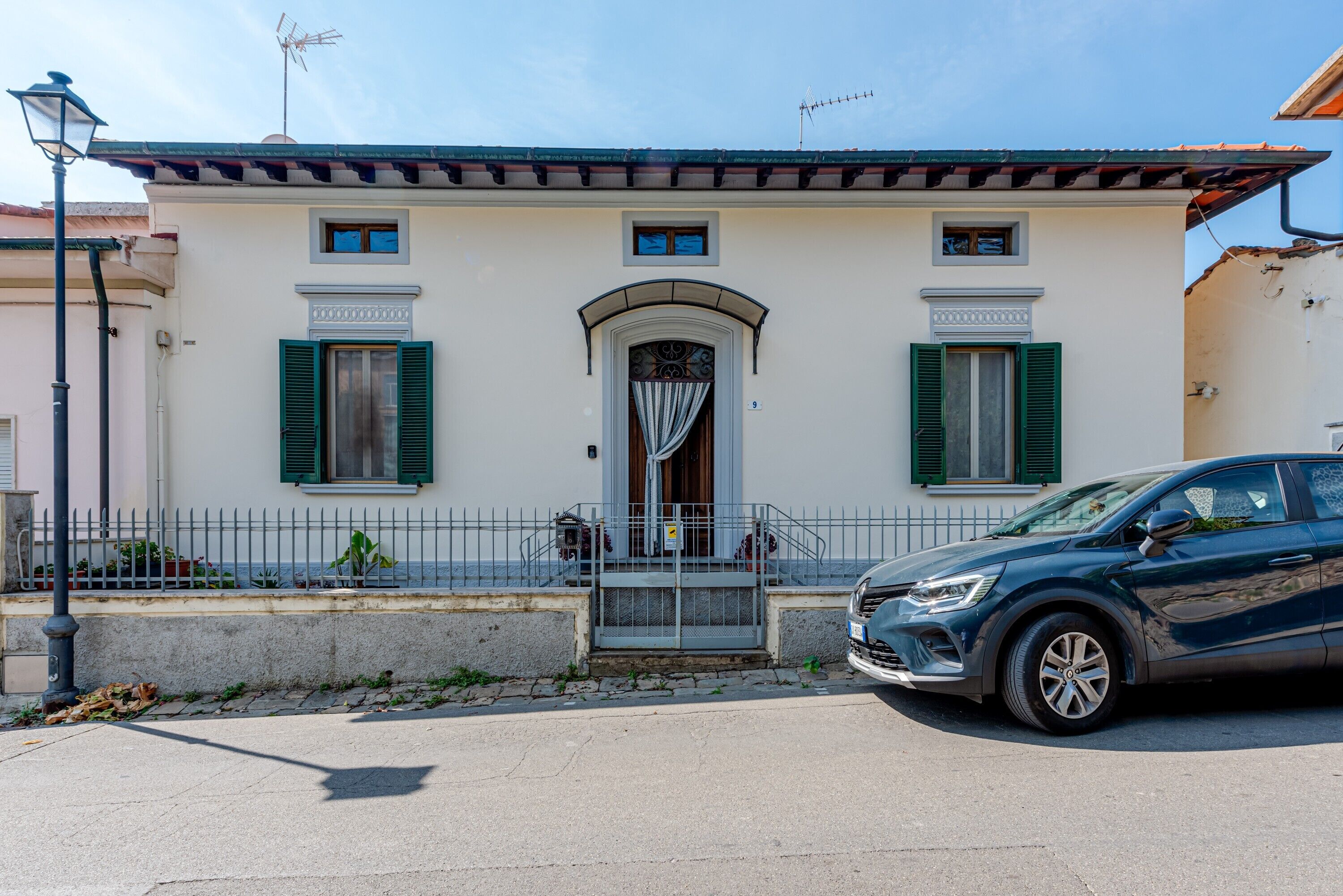 A two-story building with a central entrance, a small porch, and a car parked in front.