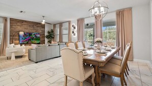 Ein modernes Wohnzimmer mit Essbereich, ausgestattet mit einem Holztisch, beigefarbenen Polsterstühlen, einem grauen Sofa und einem farbenfrohen abstrakten Gemälde an der Wand.