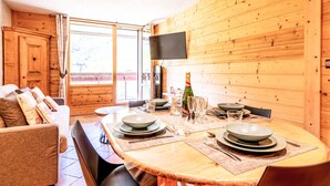 A dining area with a wooden table set for four, a sofa, and a TV mounted on the wall.