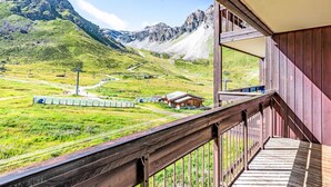 A balcony with a view of a train track, mountains, and a small building in a rural setting.