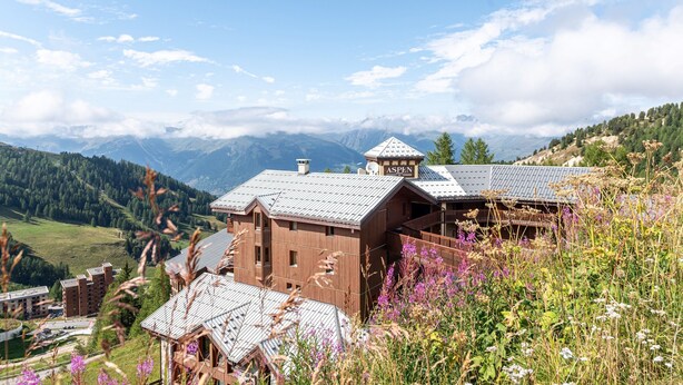 Un chalet de montagne avec une façade en bois, un télésiège et une vue sur les montagnes environnantes.