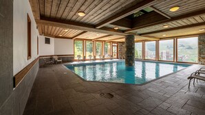Une piscine intérieure agrémentée de piliers en pierre, de poutres en bois et de grandes fenêtres offrant une vue sur l’extérieur.