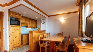 Une cuisine avec des meubles de rangement en bois, un four à micro-ondes, une horloge et une table à manger avec des chaises.