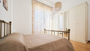 Ein Schlafzimmer mit einem Bett, einem hölzernen Kopfteil, einem weißen Kleiderschrank und einem Vorhang mit Muster.