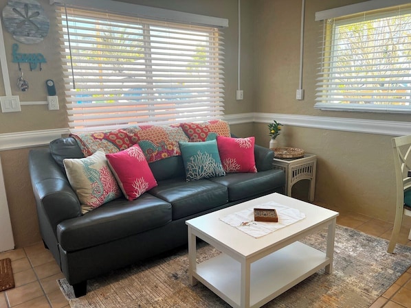 A living room with a black leather sofa, colorful cushions, a white coffee table, and a small side table with a vase.