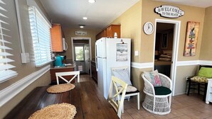 Une cuisine avec une table en bois, des chaises et un réfrigérateur. Il y a une pancarte sur le mur qui dit : « Bienvenue à la plage ».