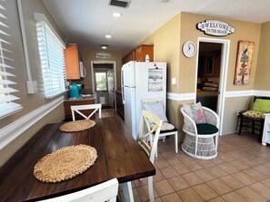 A kitchen with a wooden table, chairs, and a refrigerator. There is a sign on the wall that says "Welcome to the Beach".