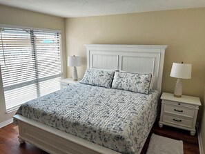 A bedroom with a bed, two nightstands, a lamp on each, and a window with blinds.