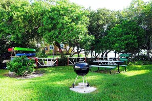 A grassy outdoor area with a barbecue grill, picnic tables, and canoes.