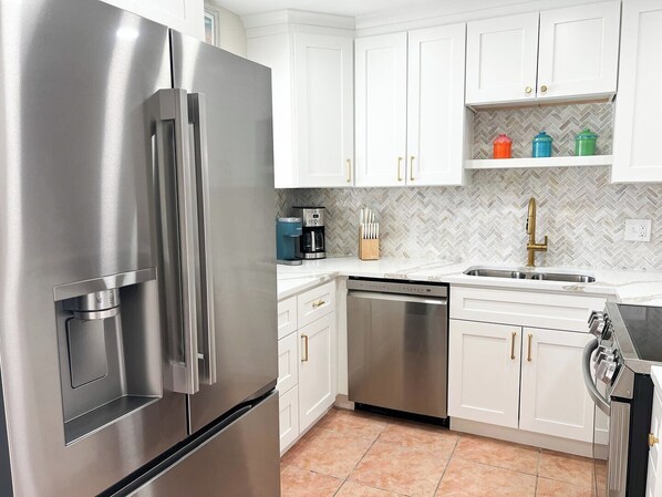 A modern kitchen with stainless steel appliances, white cabinetry, and a herringbone tile backsplash.