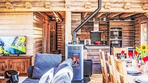 L’intérieur d’un chalet accueillant, avec un canapé, une cheminée, une table à manger dressée pour quatre personnes et un téléviseur diffusant un paysage pittoresque.
