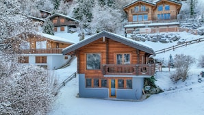 Un chalet en bois doté d’un balcon, entouré d’arbres couverts de neige et d’autres bâtiments de style chalet.