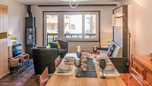 Comedor con mesa de madera dispuesta para cuatro personas, una lámpara colgante moderna y vista a través de un amplio ventanal.
