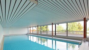 Una piscina interior con agua cristalina, ventanas amplias y suelo de baldosas.