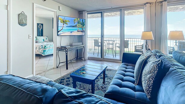 A living room with a sofa, a coffee table, a TV, and a balcony with a view of the sea. - Oceanfront Condo at Oceania Beach Club - Pool, Balcony, Sleeps 4, Walk to Flagler Ave! (New Smyrna Beach)