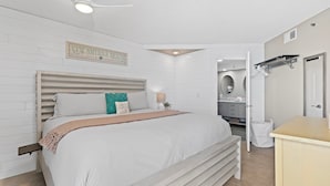Une chambre à coucher avec un lit, une table de chevet, un ventilateur de plafond et une salle de bain visible au fond.