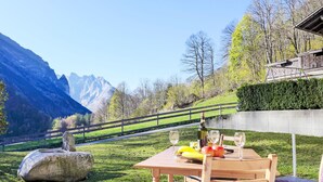 Ein Tisch im Freien, gedeckt mit einer Flasche, Gläsern, Obst und einem Stuhl.
