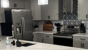 A modern kitchen with a large island, stainless steel appliances, and striped bar stools. - FOUND! Million Dollar View! Stunning Fort Meyers Beach Condo! Book Early & Save! (Fort Myers Beach)