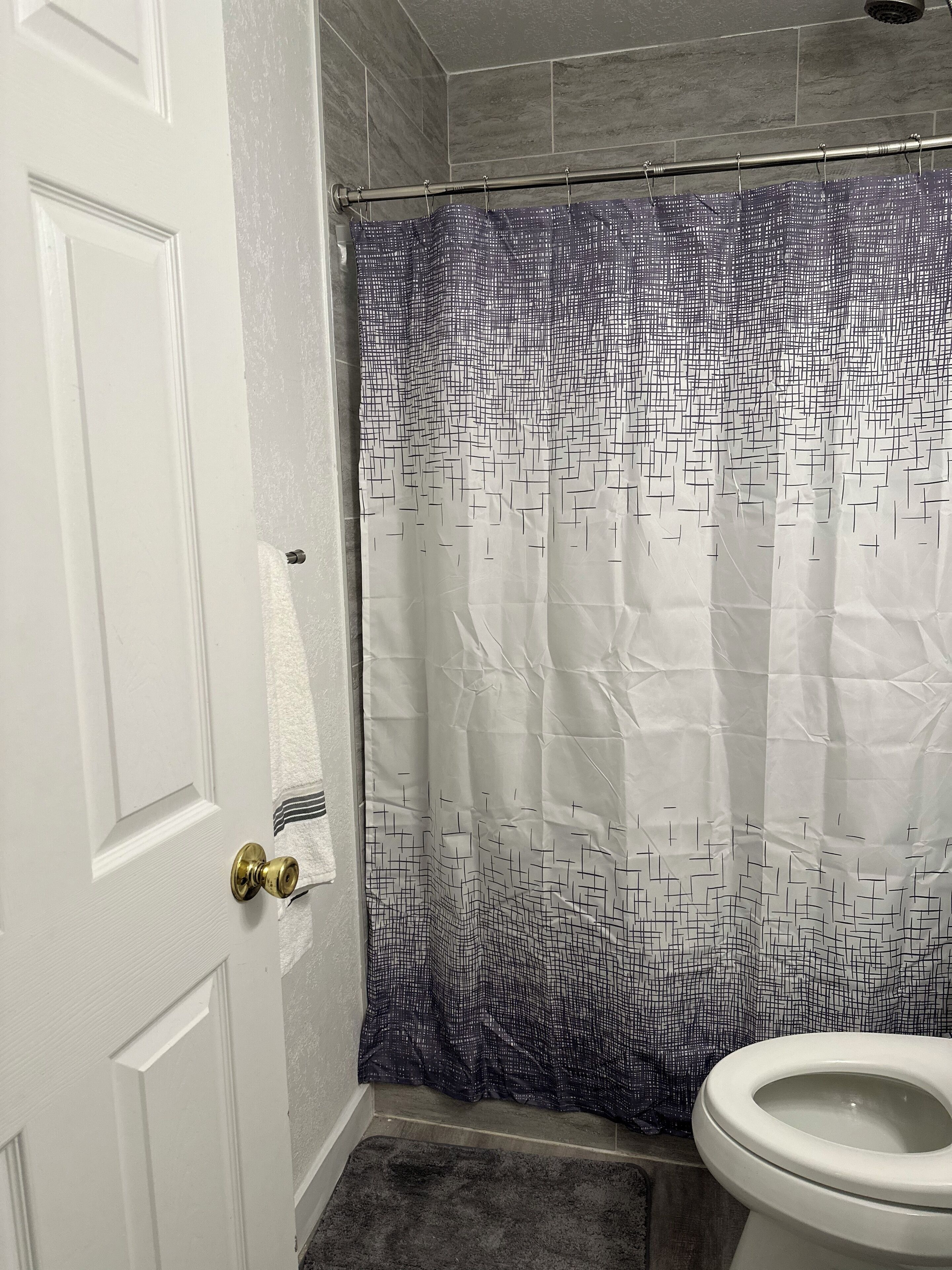 Ein Badezimmer mit einer weißen Tür, einem Duschvorhang mit geometrischem Muster und einer Toilette.