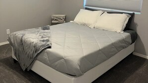 Une chambre à coucher avec un lit, une table de chevet, une lampe et une fenêtre avec des stores.
