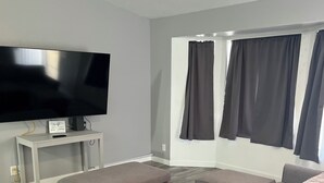 Un salon moderne avec un grand canapé d’angle, un téléviseur à écran plat posé sur un meuble et un ventilateur de plafond.