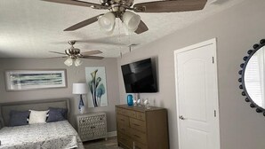 Un dormitorio con cama, cómoda, televisor, ventilador de techo y una puerta.