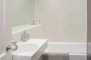 A bathroom with a white sink, a mirror, and toiletries on a shelf.