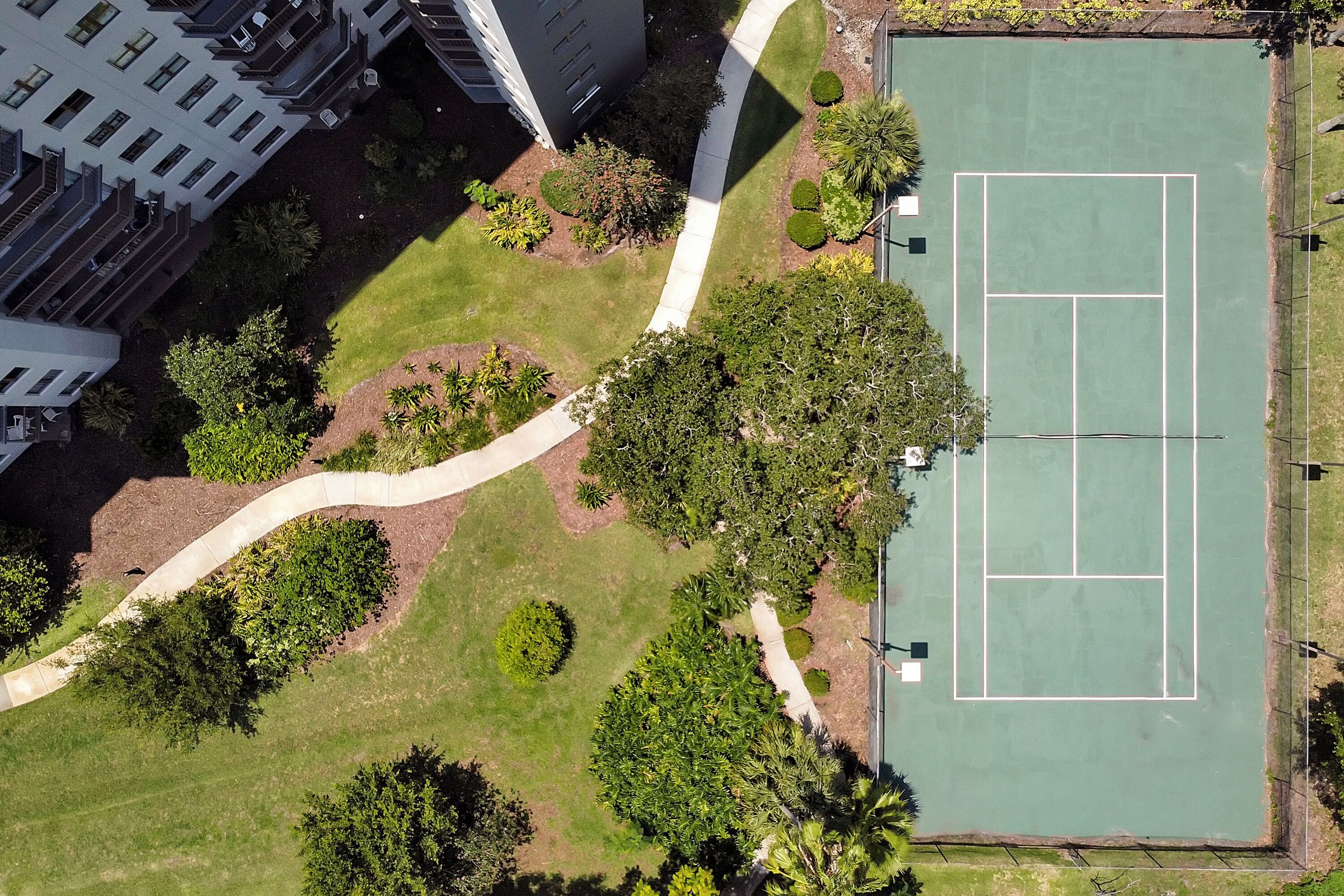 Vista aérea de una cancha de tenis rodeada de zonas ajardinadas y edificios.