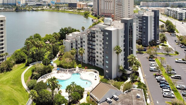 A high-rise hotel with a swimming pool surrounded by greenery, located near a body of water and a parking lot. - Premium Condos near Universal Studios (Orlando)