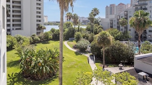 A residential area with a tall palm tree, a grassy lawn, and a pathway leading to a building with a pool. - Premium Condos near Universal Studios (Orlando)