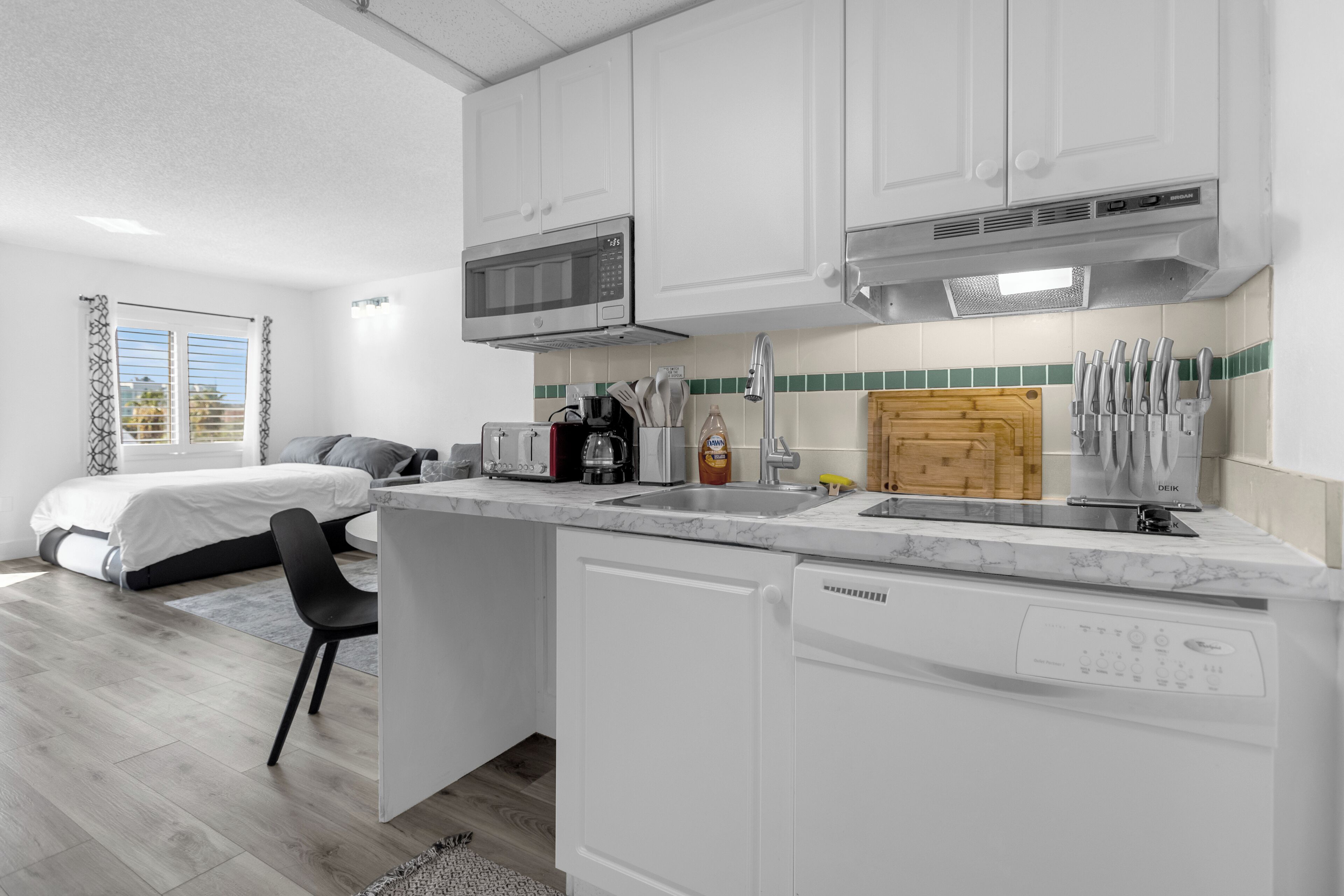 A compact kitchen with white cabinets, a microwave, a dishwasher, and a coffee maker.