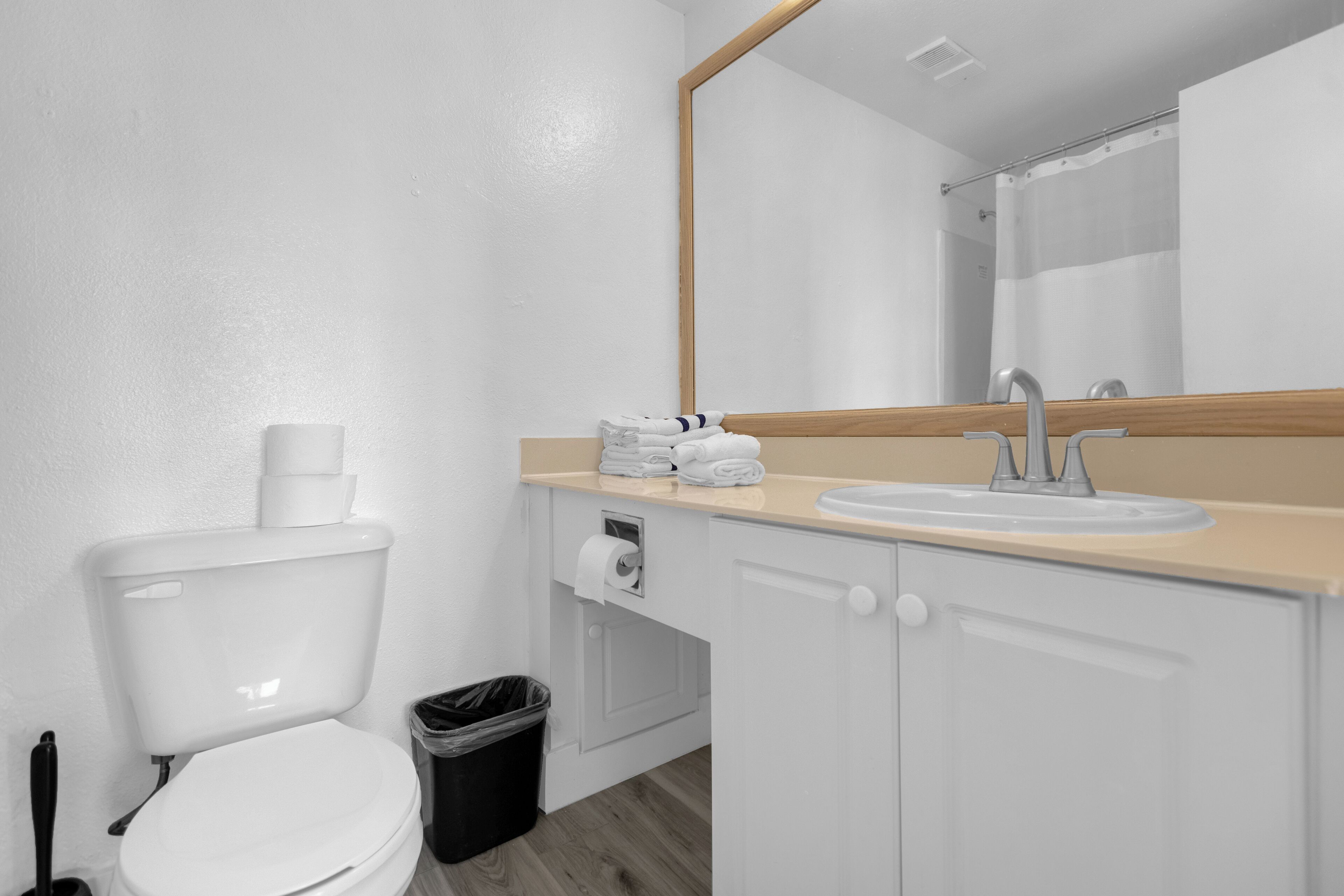 A bathroom with a toilet, sink, mirror, and a trash bin.