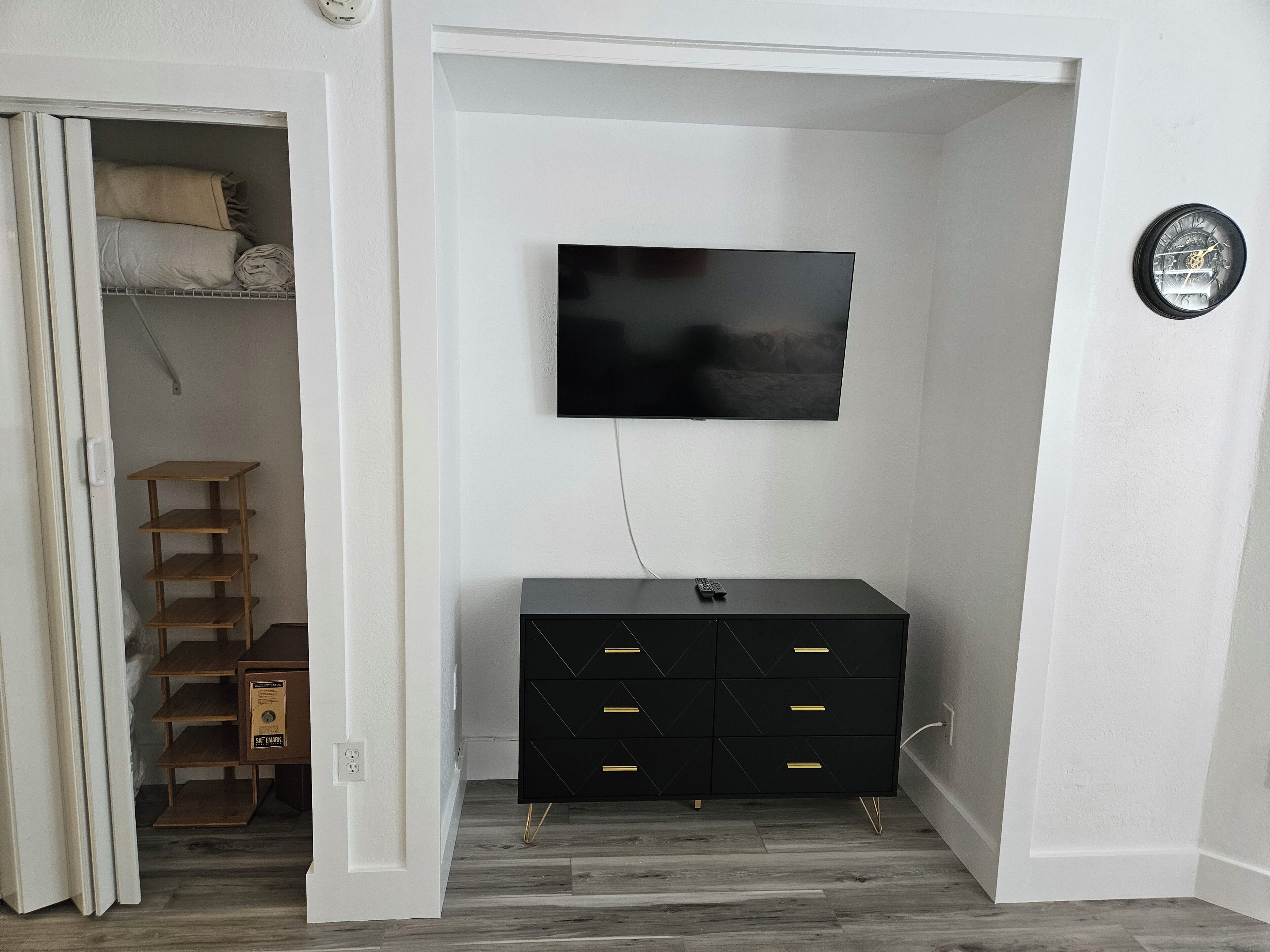 A room with a black dresser, a TV mounted on the wall, and a clock on the wall.
