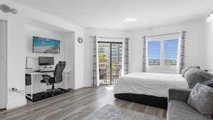 A modern bedroom with a bed, a desk with a computer, and a view of the outside balcony. - Premium Condos near Universal Studios (Orlando)