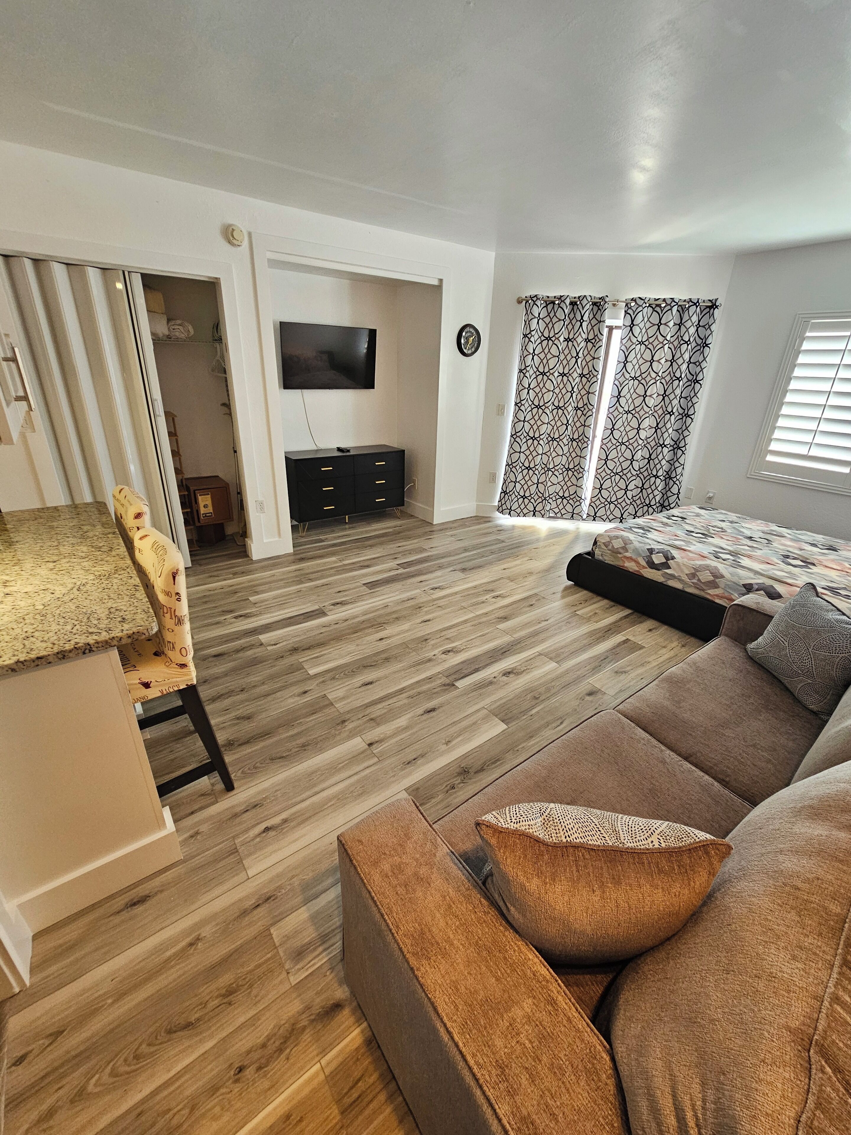 A modern living room with a wooden floor, a sofa, a TV, and a dining area with a patterned chair.