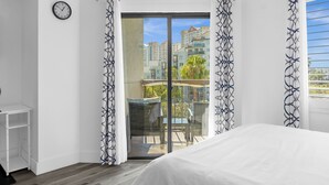 A hotel room with a balcony, a bed, a chair, a small table, and a clock on the wall. - Premium Condos near Universal Studios (Orlando)