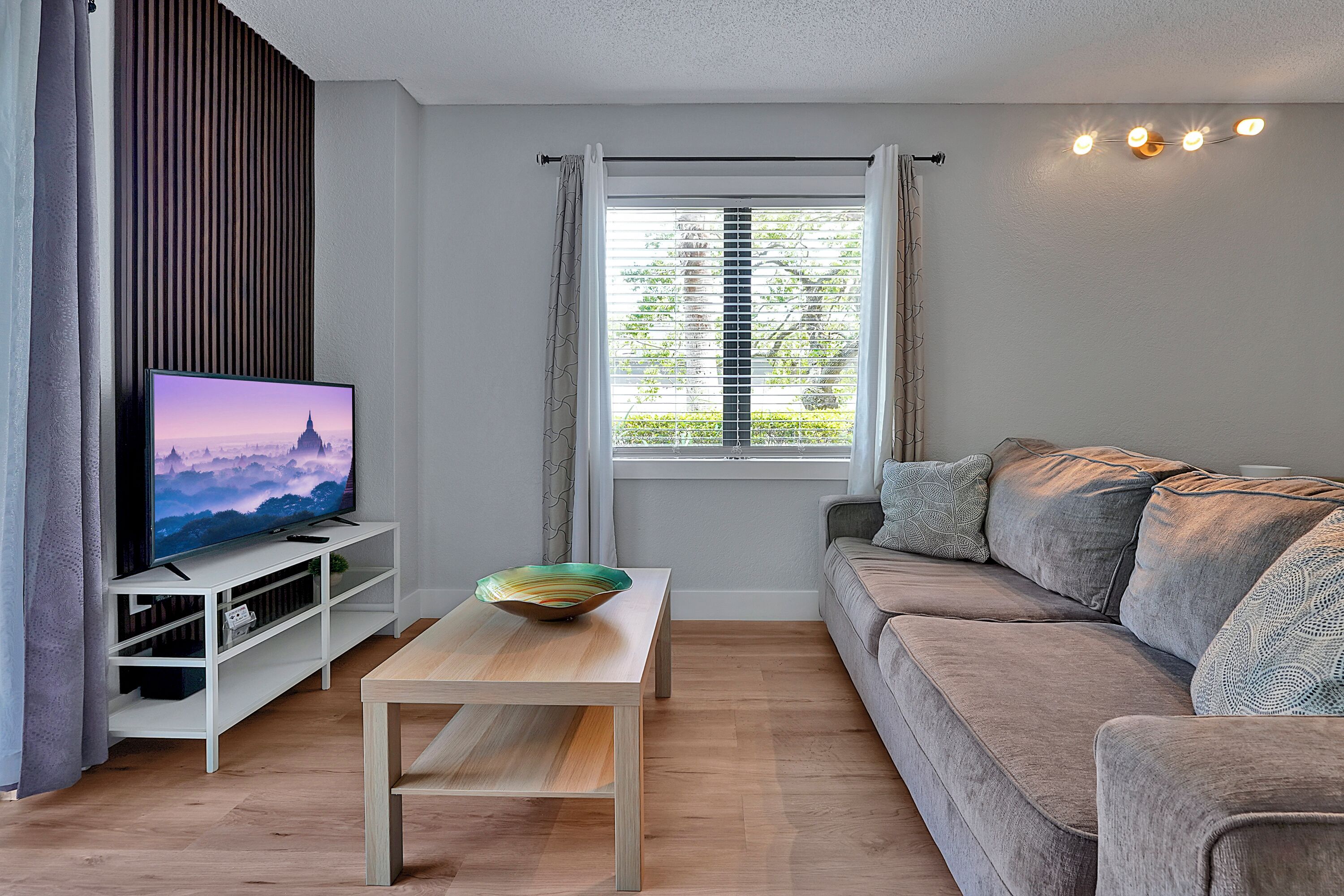 Un salon moderne avec un téléviseur à écran plat, une table basse en bois et un canapé gris.